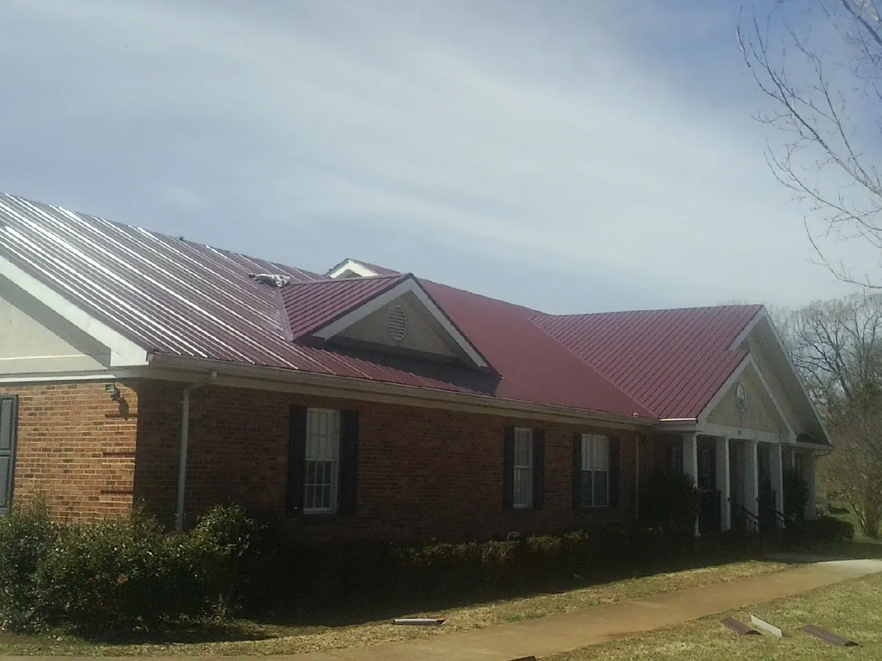 Red metal roof with gabled entries on a long brick building, from a Hail Damage Roof Repair job in Goreville