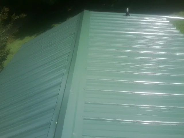 New green metal panels meeting at the ridge of a roof — Flat Roof Repair work by our crew in Goreville