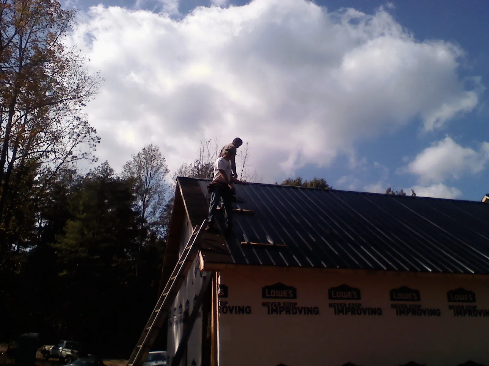 Roofer fastening dark metal panels high against a cloudy sky, from a Roof Inspection job in Goreville