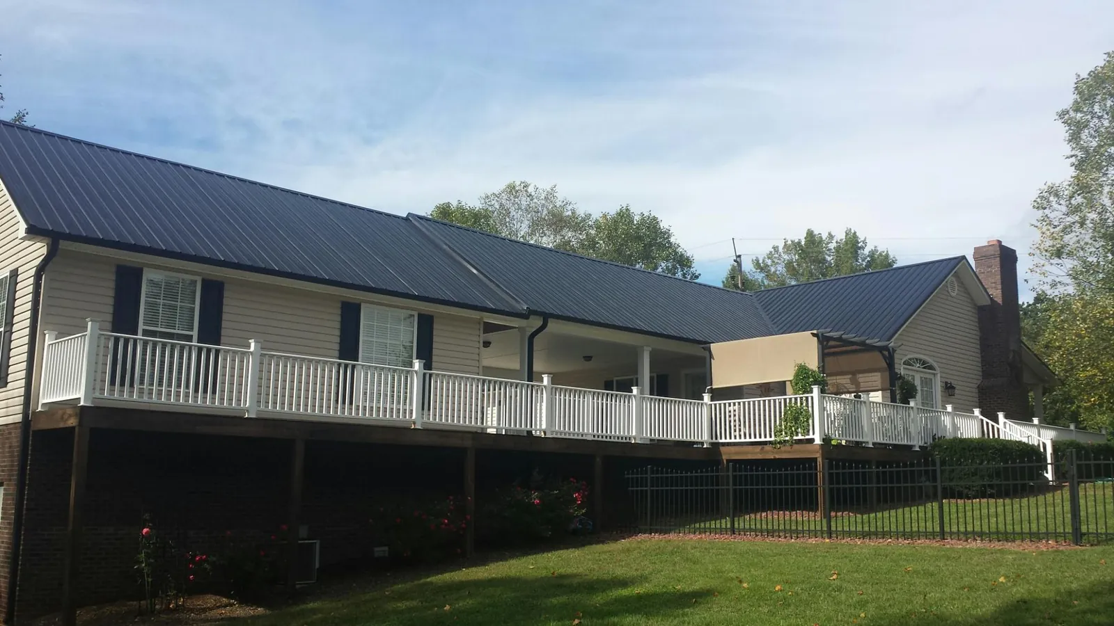 Black metal roof above a long white railed deck on a hillside home in Goreville