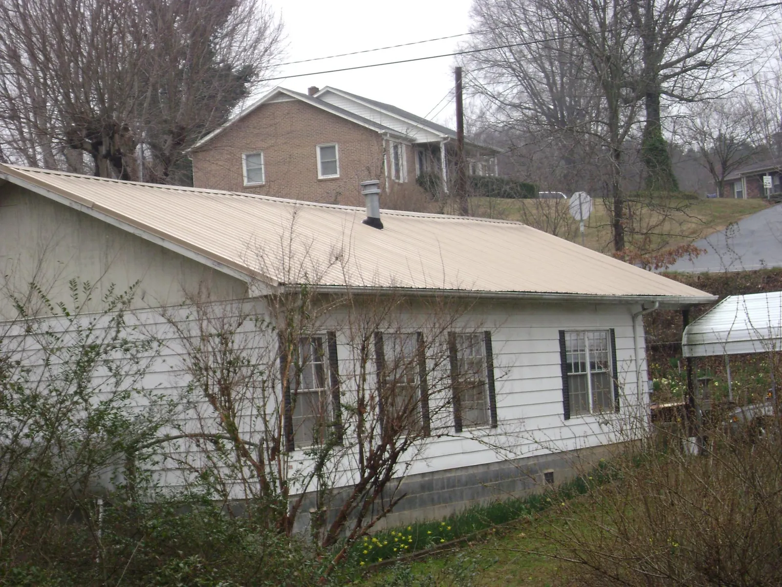 Tan metal roof on a white sided house set into a hillside — Commercial Roofing by Roofing Brothers in Goreville
